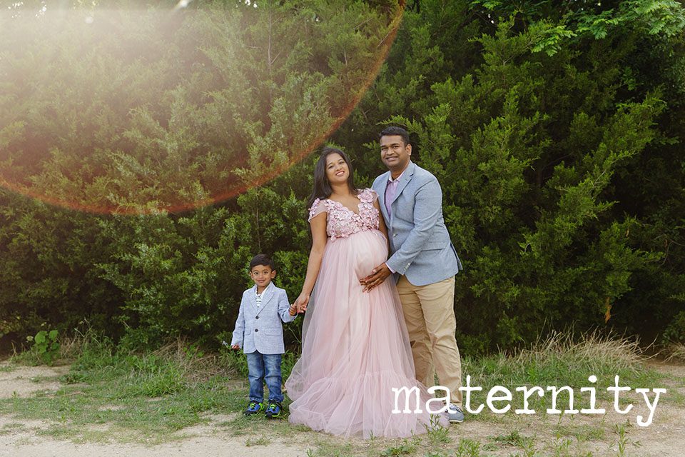 pregnant woman in pink dress with her husband and young son, in front of a row of trees, plano maternity photography