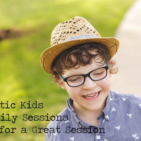 a young boy in a blue shirt, glasses and straw hat with brown curly hair, looking down with the text that says 'autistic kids in family photos: tips for a great session"
